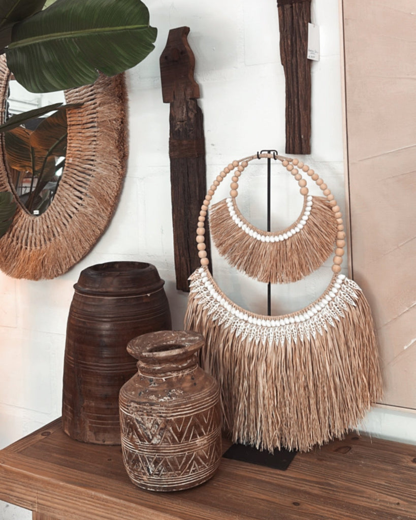 Decorative items including a beaded necklace with fringe, wooden vases, and a wall mirror on a wooden surface.
