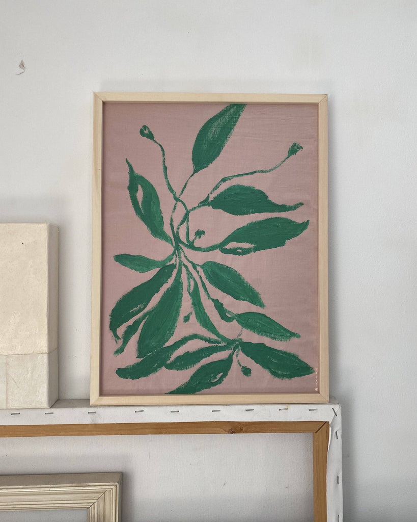 Framed artwork with green leaf design on a pink background, displayed on a shelf.
