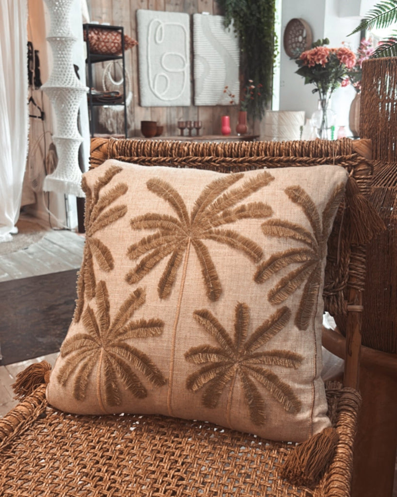 Decorative pillow with leaf pattern on a wicker chair in a room setting.