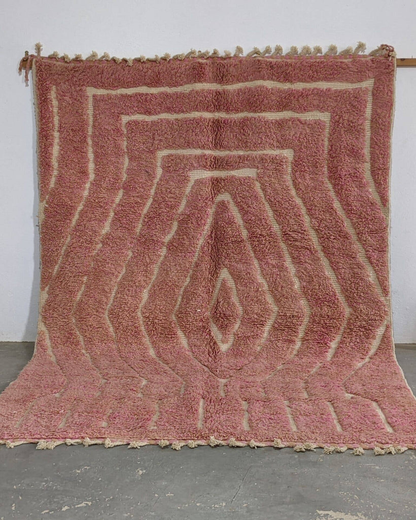 Pink geometric patterned rug on a gray floor with a white wall background