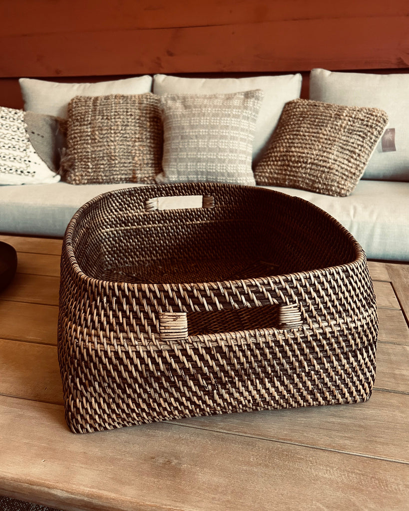 Woven basket on a wooden surface with a sofa and pillows in the background