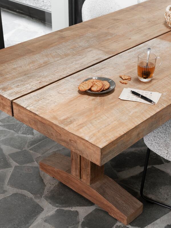 Wooden dining table with a glass of tea, cookies, and a pen on a stone floor.