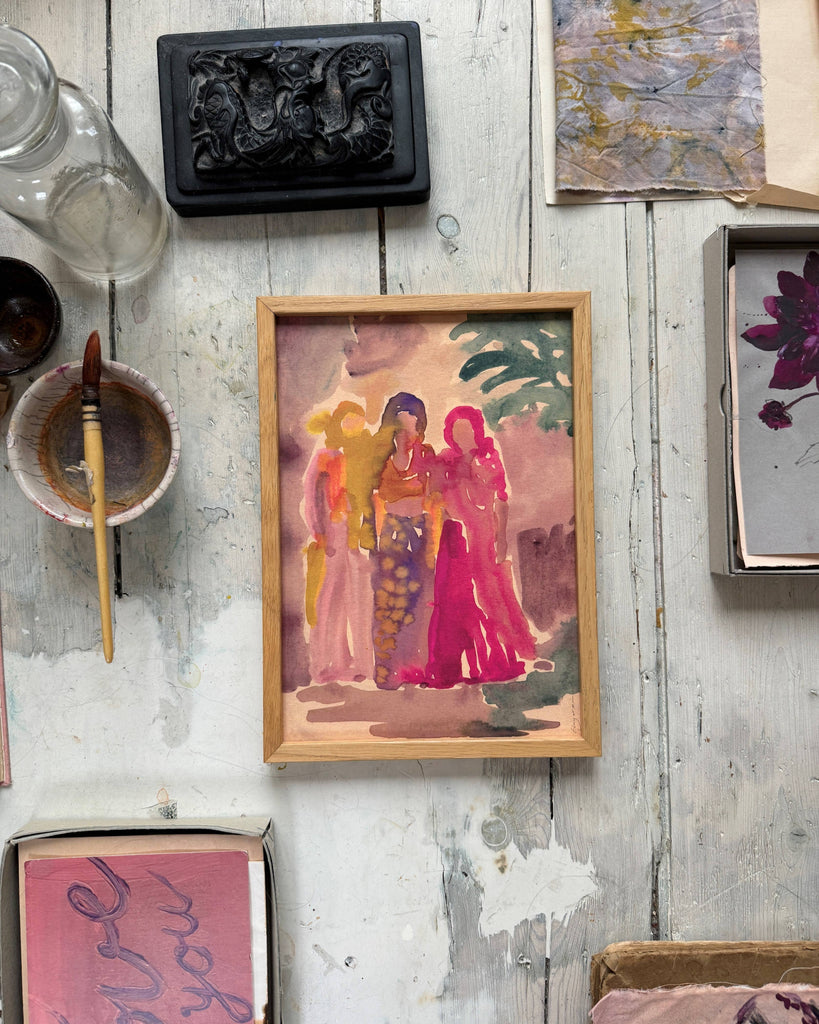 Framed artwork of three figures on a rustic wooden surface with art supplies.