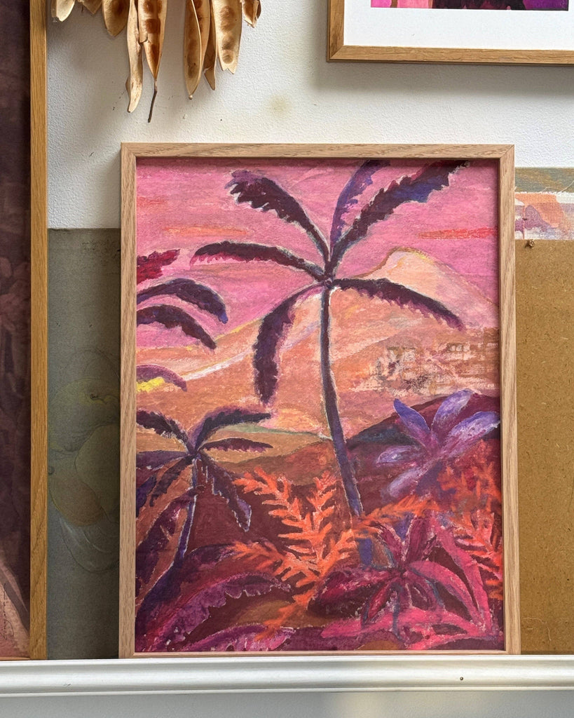 Framed tropical landscape painting with palm trees on a wall.