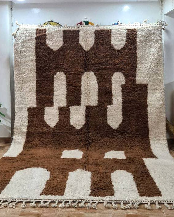 Brown and white patterned rug on a wooden floor with a plant and chair in the background.