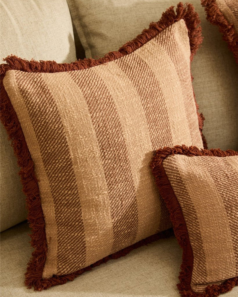 Textured brown and beige pillow with frayed edges on a beige sofa.