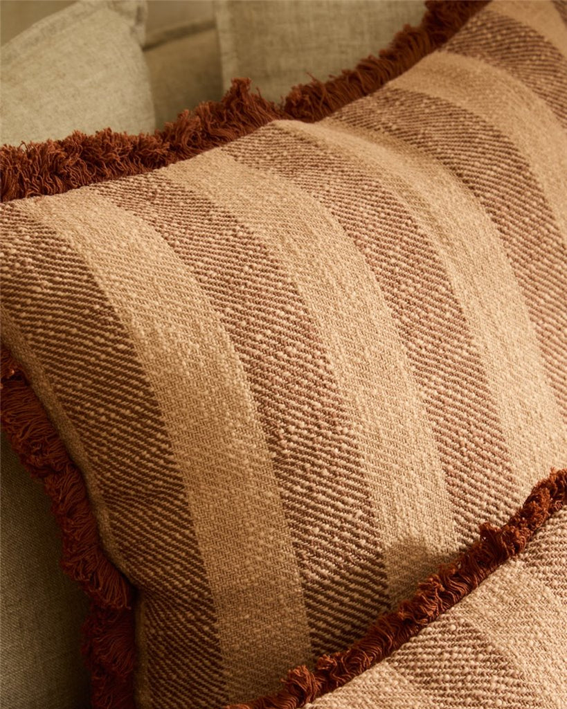 Close-up of a textured pillow with brown trim on a neutral background