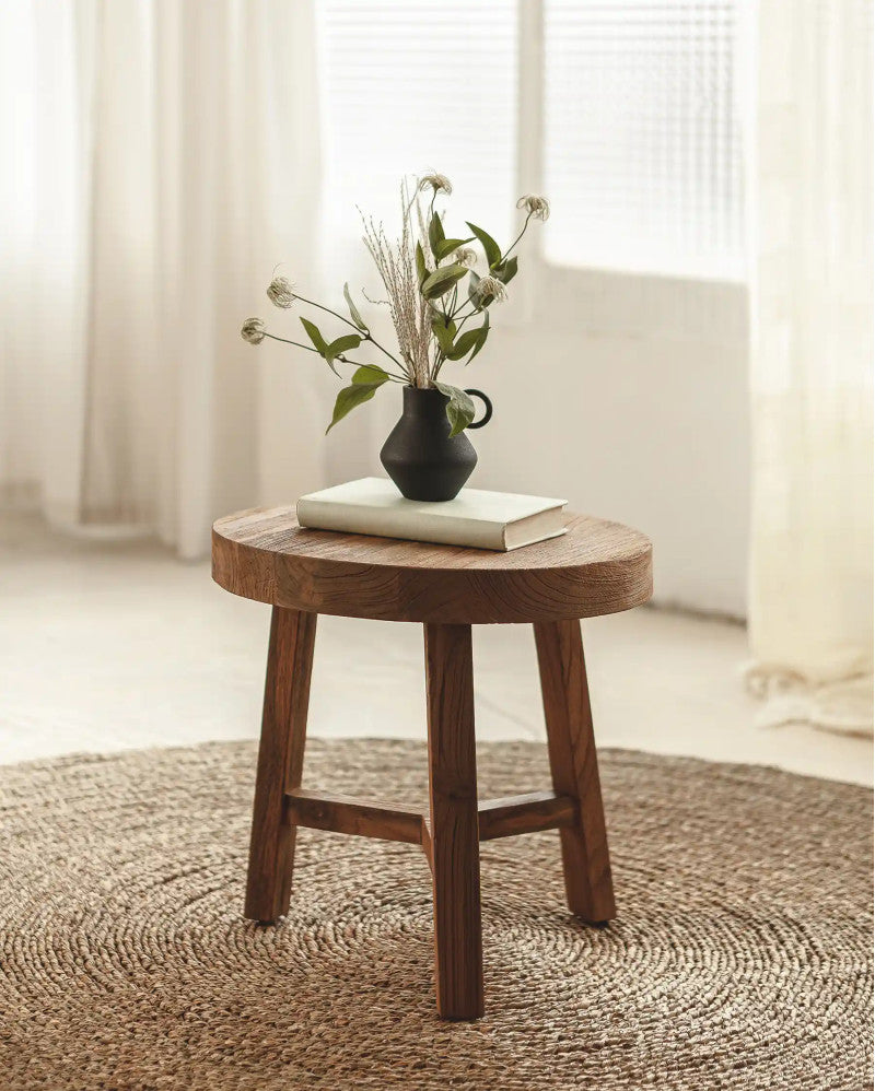 Wooden stool with a black vase and book on a textured rug