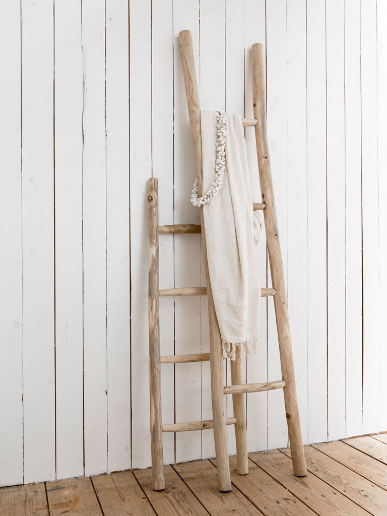 Wooden ladder against a white paneled wall with a white blanket draped over it.