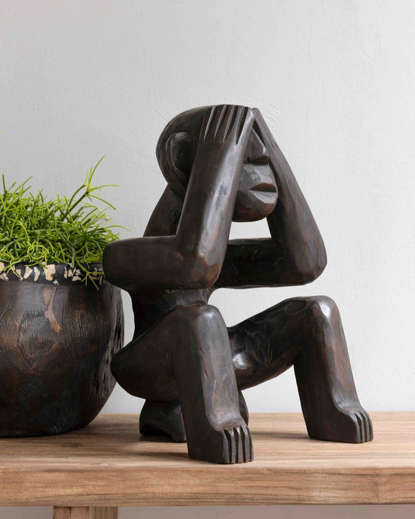 Abstract sculpture on a wooden surface with a plant in the background