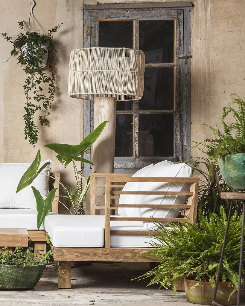 Outdoor furniture set with wooden chairs and white cushions, surrounded by plants against a rustic wall.