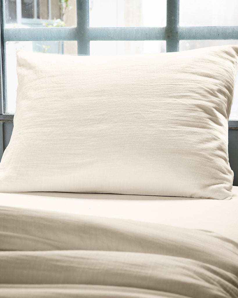 Beige pillow and duvet on a bed with a window in the background