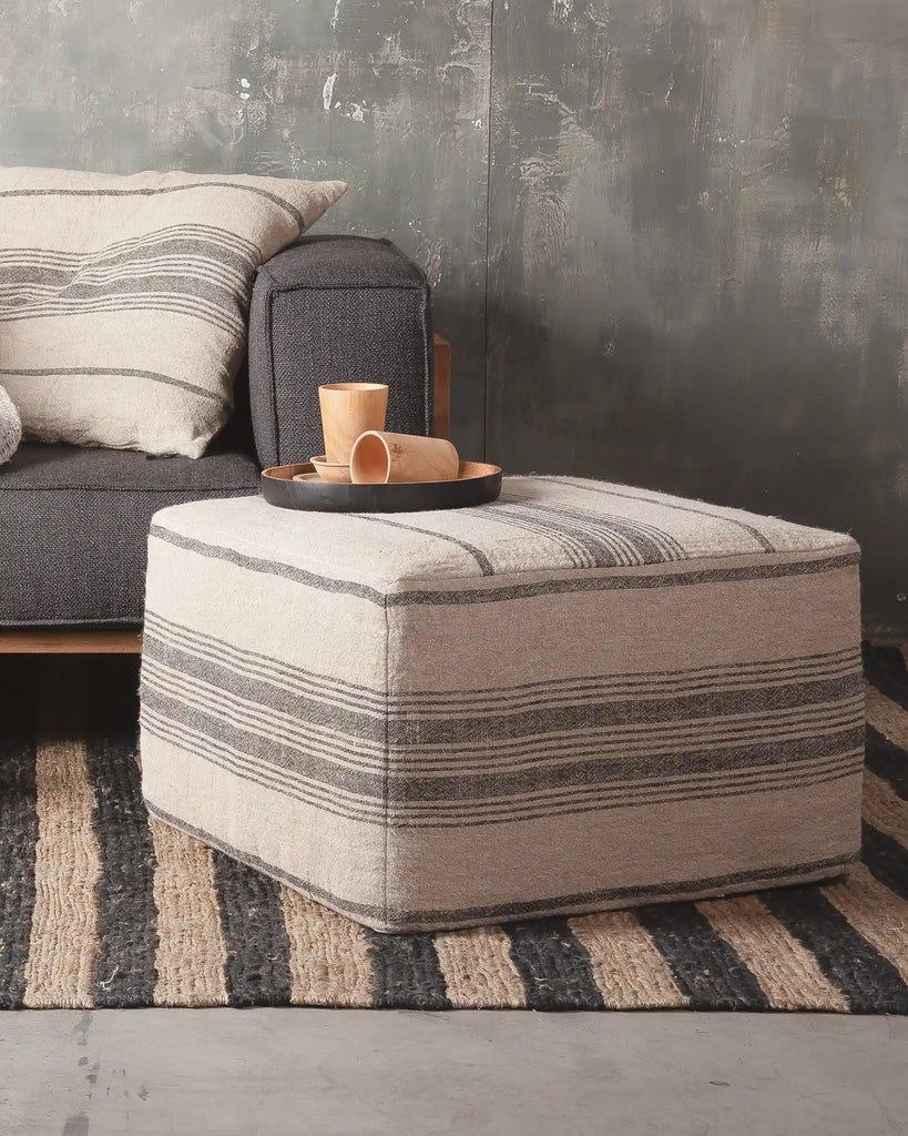 Striped ottoman in a living room setting with a sofa and coffee table.